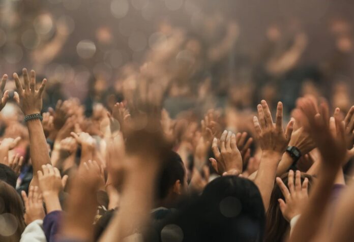 Interior de una iglesia llena de fieles con las manos levantadas durante una celebración cristiana, expresión de fe, emoción y participación comunitaria.