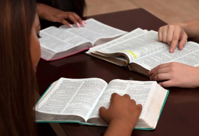 Personas reunidas leyendo y estudiando la Biblia en una mesa, señalando pasajes del texto.